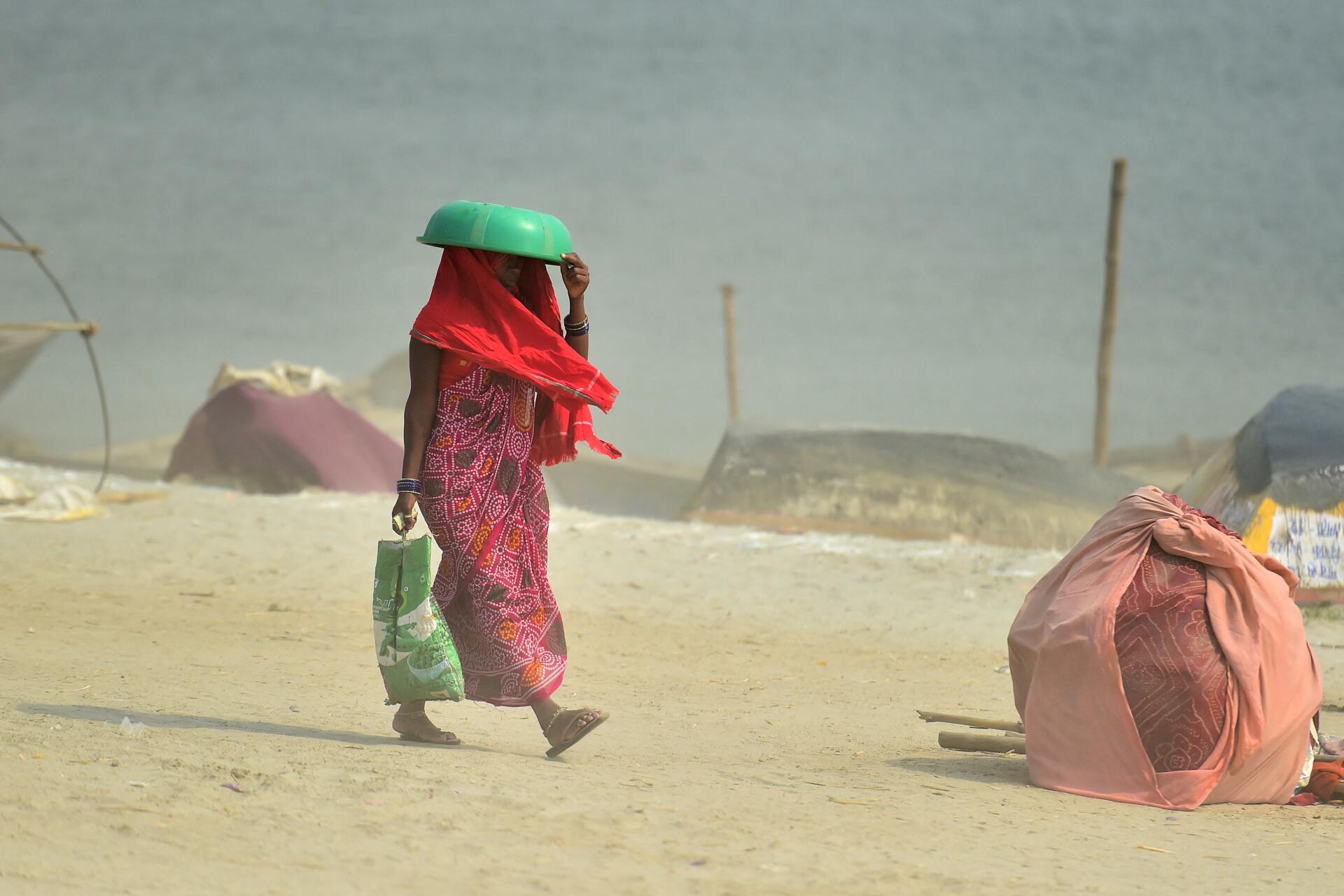 A woman covers her head with a plastic bowl as she walks in Allahabad on April 30, 2022 near Sangam, the confluence of the Ganges, Yamuna and mythical Saraswati rivers.