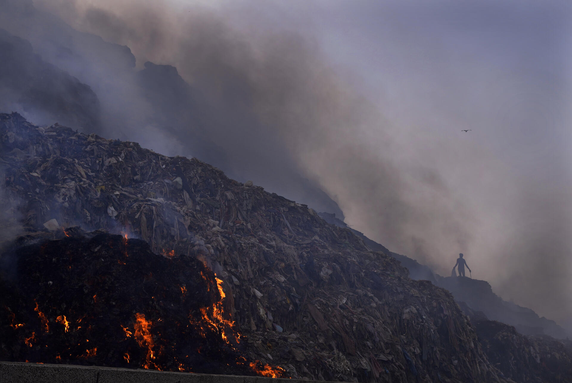 A rag collector searches for reusable items as a fire breaks out at the Bhalswa landfill in New Delhi on Wednesday, April 27, 2022. 