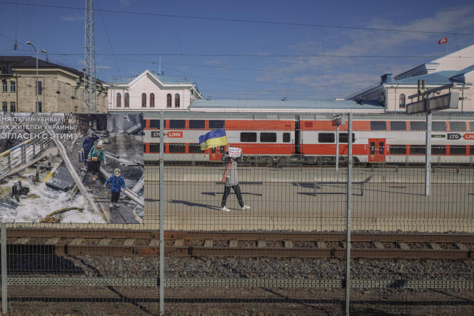 On April 21, 2022, at the Vilnius (Lithuania) train station. A woman walks behind pictures of the war in Ukraine with a flag and a sign calling for Russians to leave the country, while the train connecting Belarus and the Russian enclave of Kaliningrad is stopped.