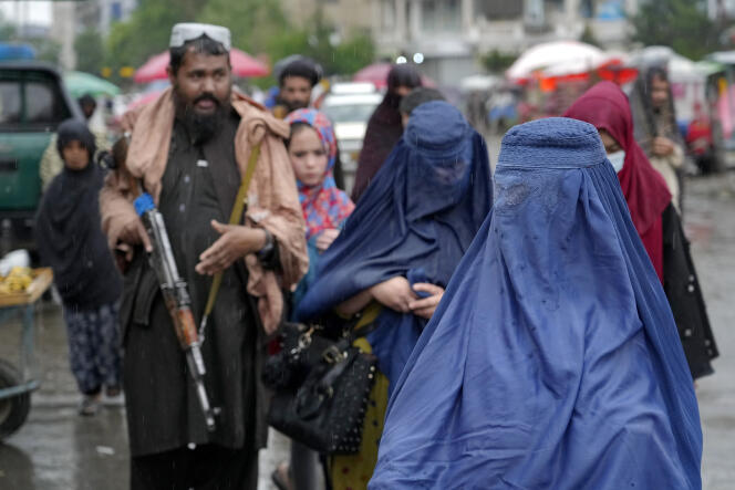 Women wearing burkas and accompanied by Taliban guards walk through a market in Kabul on May 3, 2022.