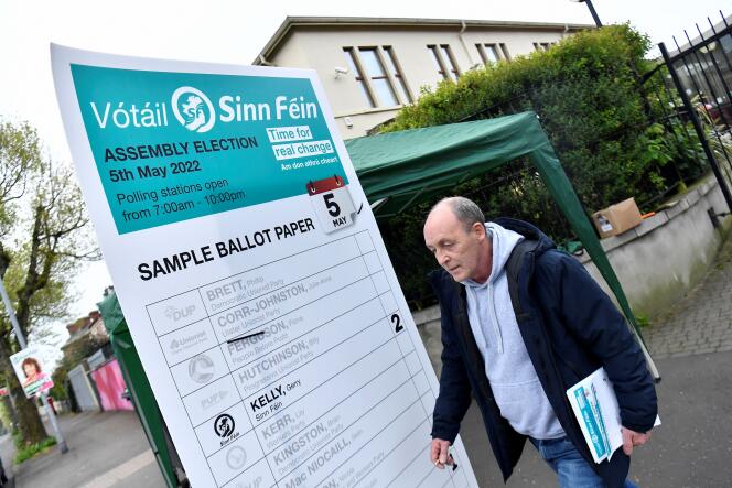 Seorang aktivis Sinn Fein berdiri di luar tempat pemungutan suara, di depan contoh surat suara yang menunjukkan siapa yang harus dipilih untuk memilih nasionalis, di Belfast, Irlandia Utara, 5 Mei 2022. 