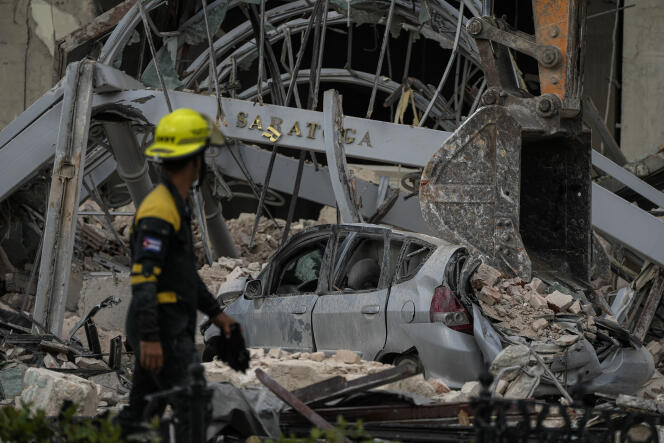 A member of a rescue team walks past a crushed car at the site of a deadly explosion that destroyed the five-star Hotel Saratoga, in Havana, Cuba, Friday, May 6, 2022.