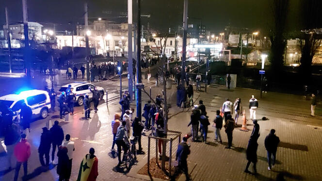 Sur cette capture d’écran d’une vidéo tournée le 6 février 2022, place Georges-Arnold, à Saint-Denis (Seine-Saint-Denis), on voit un policier en civil, devant la voiture de police (en haut à gauche), brandir une grenade lacrymogène, avant de la jeter en criant « Messieurs, cadeau ! » 