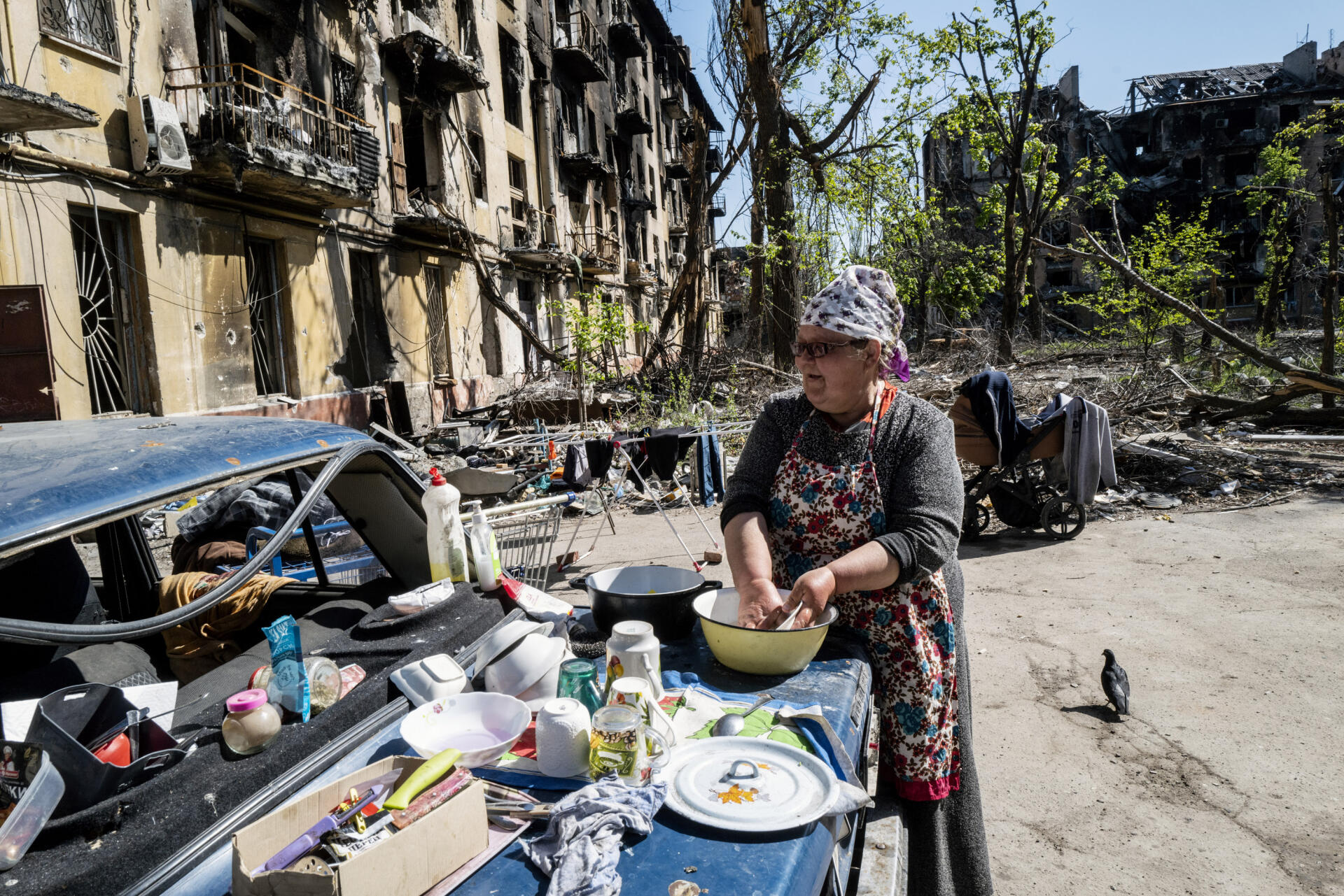 Une femme fait la vaisselle sur le coffre d’une voiture, au pied d’un immeuble dévasté par les bombardements, à Marioupol (Ukraine), le 8 mai 2022.