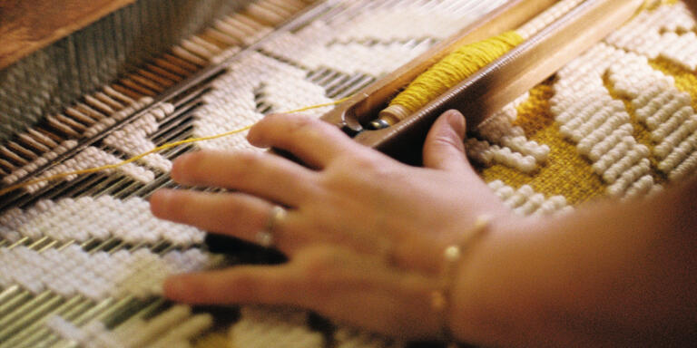 A weaver weaving the Verne model on a creel loom, recognizable by its bobbin placed at the beginning of the loom.
