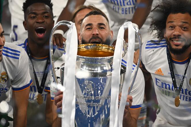 Karim Benzema, surrounded by Real Madrid teammates, lifts the Champions League trophy after the victory over Liverpool at the Stade de France on May 28, 2022.