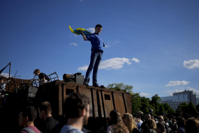 Un jeune homme brandit un drapeau ukrainien sur un char russe détruit, symbole de cette guerre, lors des célébrations de la fête de Kiev, dimanche 29 mai 2022.