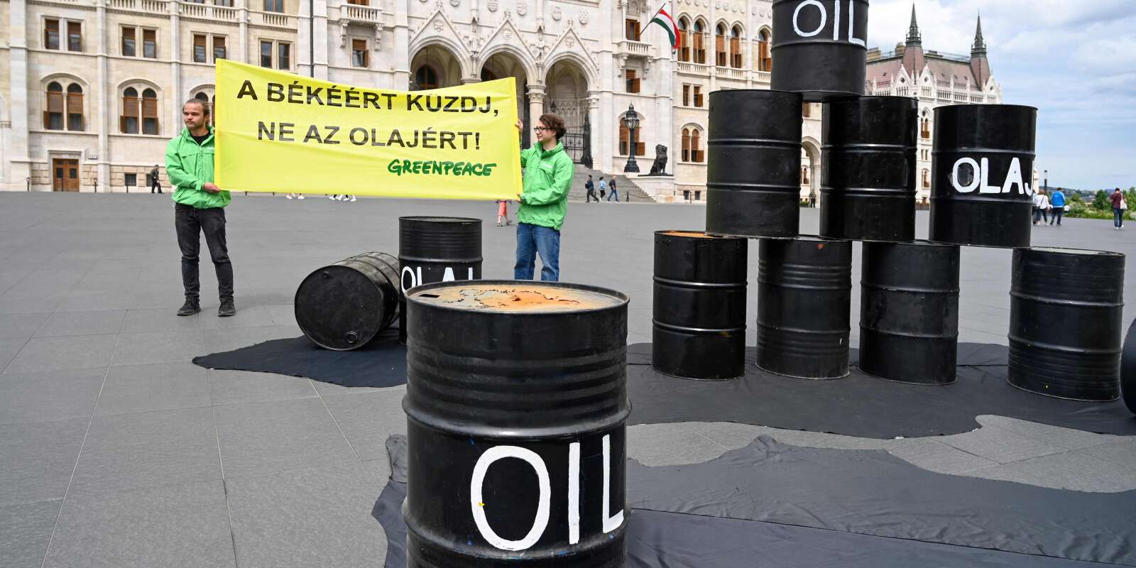 une banderole (« Luttez pour la paix, pas pour le pétrole ») est déployée, et des barils de pétrole sont disposés par des militants de l’association Greenpeace devant le Parlement hongrois à Budapest, le 30 mai 2022, pour exiger du gouvernement de ne pas s’opposer aux sanctions de l’Union européenne contre le pétrole russe.