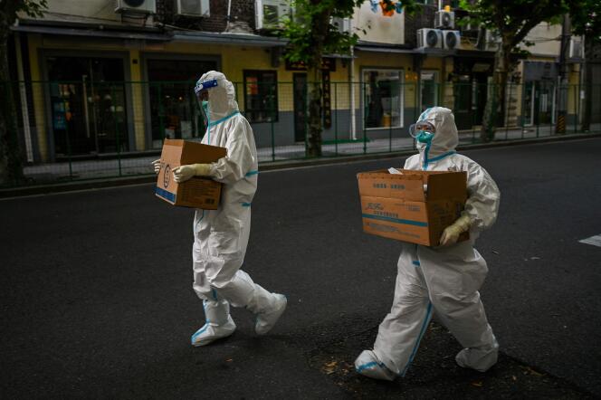 Des agents de santé portant des équipements de protection marchent dans une rue à côté d’une zone résidentielle sous confinement dans le district de Xuhui, à Shanghaï, le 8 juin 2022. 