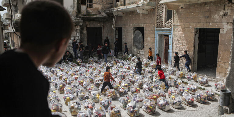 A boy watches as children run between humanitarian food aid packages being handed over by a volunteer team of first responders to locals in the town of al-Najieh in the western countryside of Syria's rebel-held northwestern Idlib province, which is currently along the frontlines with Syrian government forces, on April 6, 2022. (Photo by Aaref WATAD / AFP)