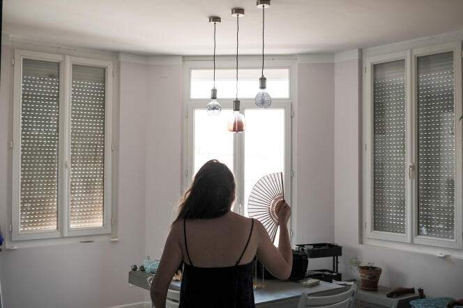 A woman cools herself with her fan in the living room of her apartment, in which the shutters are closed to limit the sun's heat, in Perpignan, June 13, 2022.