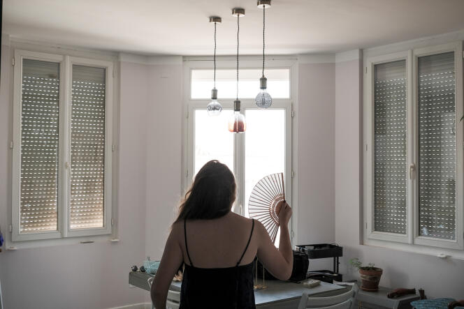 Une femme se rafraîchit a l’aide de son éventail, dans le salon de son appartement, dans lequel les volets sont fermés afin de limiter la chaleur du soleil, à Perpignan, le 13 juin 2022.