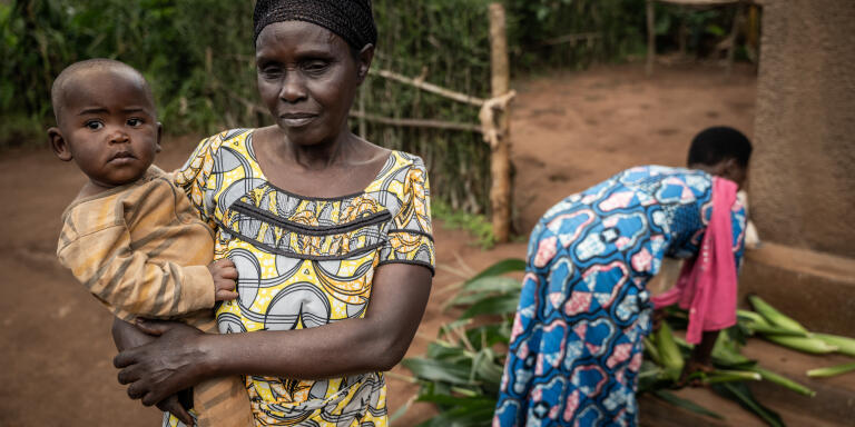 Speciose Mukanagena porte son petit fils  à Mwurire, district de Rwamagana, Est du Rwanda le 3 juin 2022. Speciose a 62 ans, quatre enfants, elle est depuis trois ans avec one acre fund (OAF). Avant d’être soutenue par OAF, elle n’utilisait pas de fertilisant pour ses plantations et parvenait tout juste à survivre de sa production. Aujourd’hui elle parvient à produire suffisamment pour nourrir sa famille et vendre le surplus, elle a pu acheter un nouveau toit pour sa maison et acheter une machine à coudre à sa fille pour devenir couturière. One acre fund fournit à crédit aux agriculteurs des graines de qualité, du fertilisant et rachète leur production à un prix fixe. Si près de 70% des rwandais vivent de l’agriculture, ce secteur ne représente qu’un tier du produit intérieur brut (PIB).