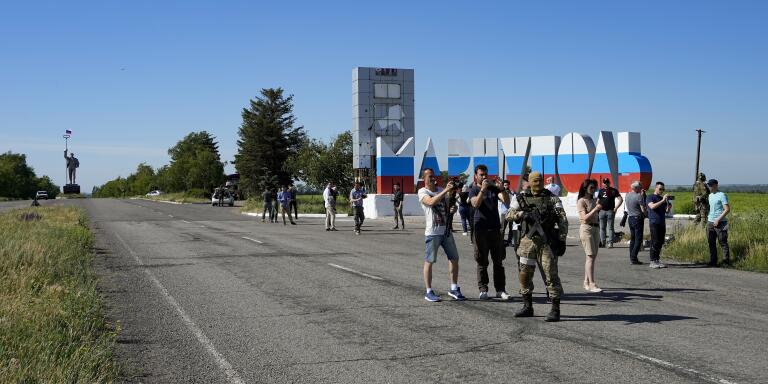 A group of foreign journalists walk past a repainted city name in the colors of the Russian flag at the entrance of Mariupol, on the territory which is under the Government of the Donetsk People's Republic control, eastern Ukraine, Sunday, June 12, 2022. This photo was taken during a trip organized by the Russian Ministry of Defense. (AP Photo)