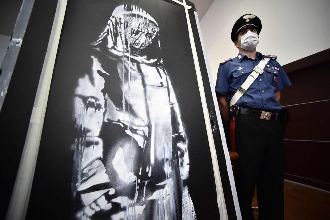Un policier monte la garde près de l’œuvre d’art de Banksy volée au Bataclan à Paris en 2019, L’Aquila (Italie), le 11 juin 2020.