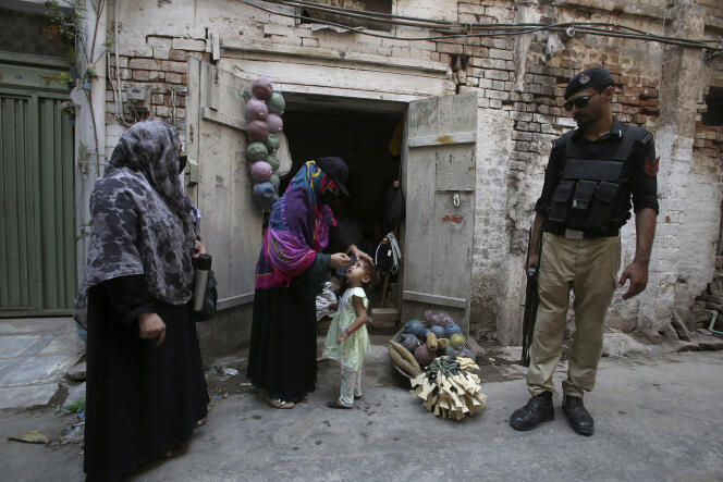A police officer stands guard as a health worker administers a polio vaccine to a child in Peshawar, Pakistan, June 27, 2022.