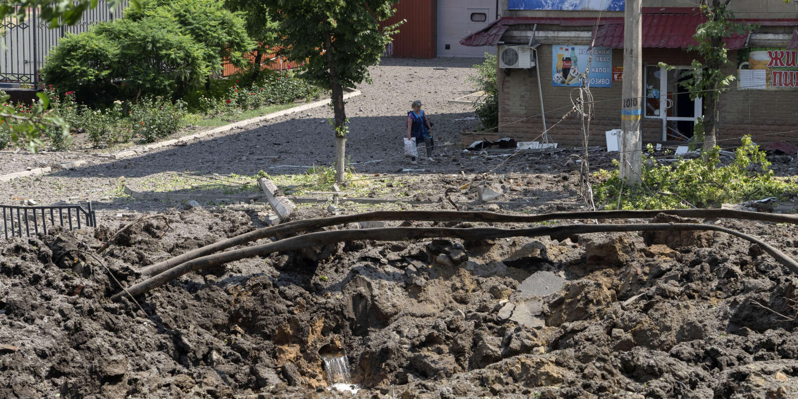 Une femme passe devant un énorme cratère laissé par une roquette russe dans le centre-ville de Bakhmout, dans la région de Donetsk en Ukraine, le 1er juillet 2022.