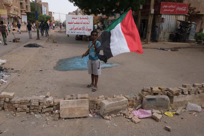 Un niño se para frente a la 'República Democrática de Al-Diyum'.  Las calles de este distrito están erizadas de barricadas.  De esta avenida parten cada semana las procesiones en dirección al palacio presidencial.  Esta vez, los comités de resistencia prefirieron organizar un plantón.