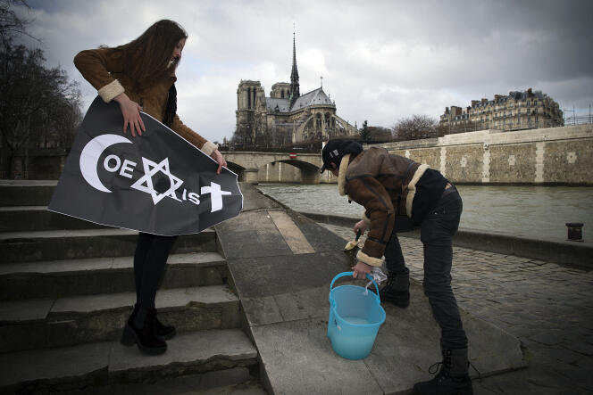 Deux jeunes femmes collent une affiche de l’artiste de rue français Combo, le 8 février 2015, sur le quai de la Tournelle, à Paris.