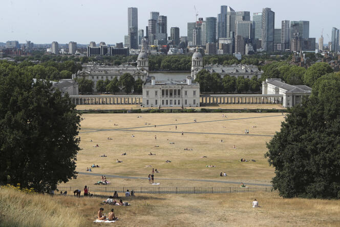People sit on the sun-parched grass in Greenwich Park with the Maritime museum and Canary Wharf financial district in the background in London, Sunday July 17, 2022. 