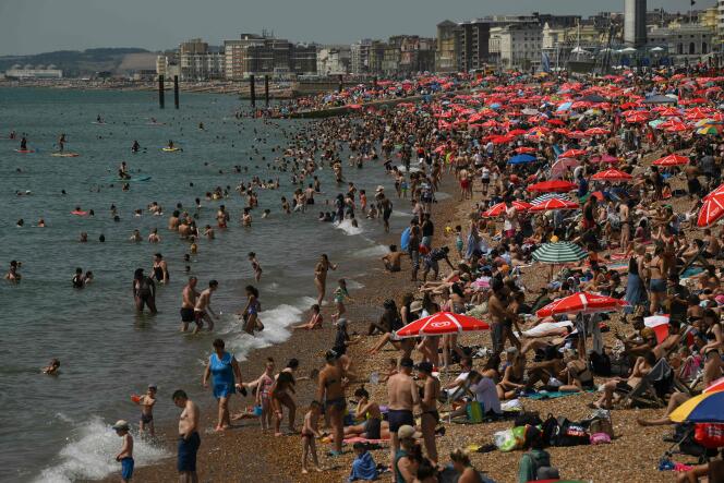 Beachgoers sit in the sun on the beach and paddle in the sea at Brighton, southern England on July 17, 2022. 