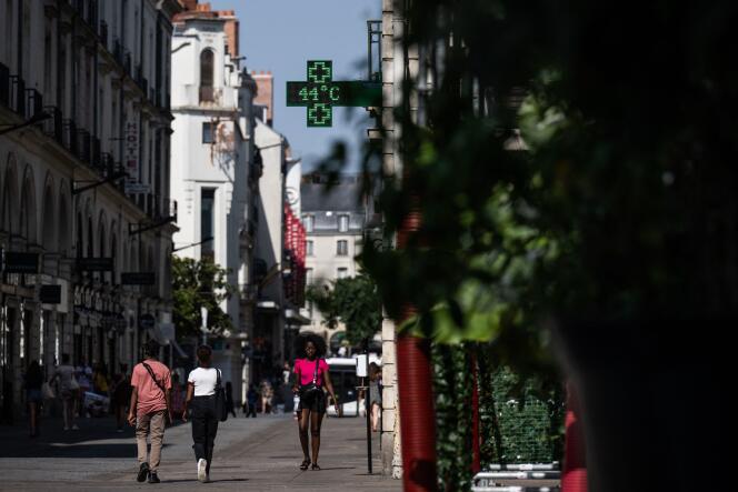 People walk down a street in Nantes, on July 18, 2022, as a pharmacy lighted sign shows the temperature off 44 degrees celsius. 