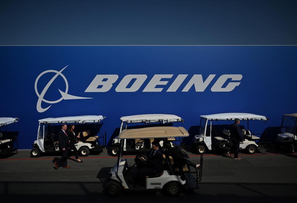 Visitors walk past a Boeing board and car carts during the Farnborough Airshow, in Farnborough, on July 18, 2022. (Photo by JUSTIN TALLIS / AFP)