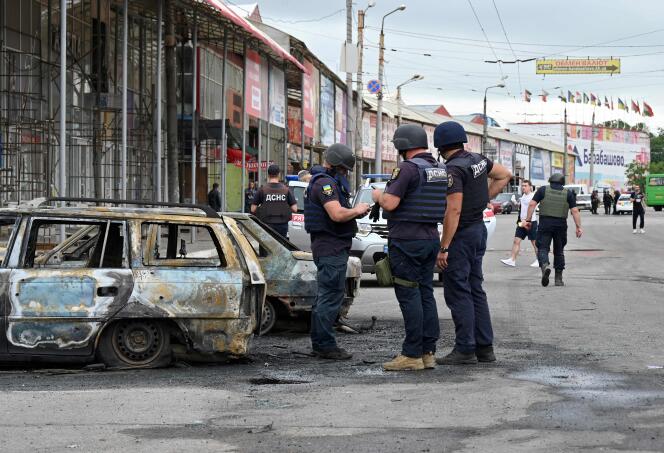 Rescuers stand next to burnt car after a Russian rocket strike in one of the districts of Kharkiv on July 21, 2022 amid the Russian invasion of Ukraine.