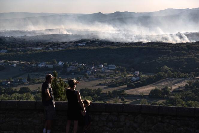Residents look at the plumes of smoke rising above a forest, near Vogüé, in Ardèche, on July 27, 2022.