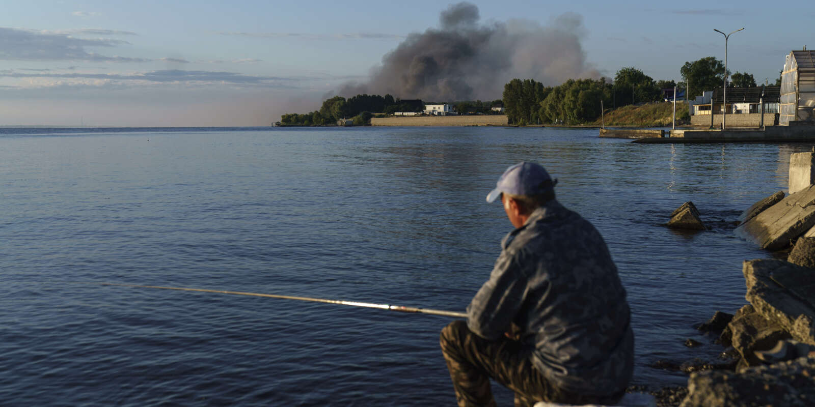 Un pêcheur à la ligne regarde la fumée s’échapper après une frappe de missile russe dans la banlieue de Kiev. Le 28 juillet 2022.