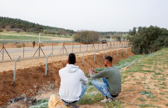 Des Palestiniens regardent les forces de sécurité israéliennes boucher des trous dans une clôture frontalière près du poste de contrôle de Mitar, au sud d'Hébron, en Cisjordanie, le 3 avril 2022. Des milliers de travailleurs palestiniens y passaient quotidiennement pour entrer illégalement dans les zones israéliennes pour travailler.