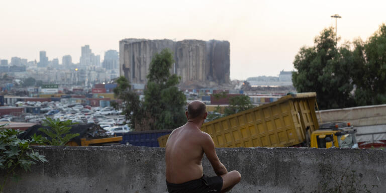 A man, sitting on a block of cement, watches as fire and smoke billow from the silos at the port of Beirut, Lebanon, Tuesday, August 2, 2022. On Sunday July 31, part of the silos collapsed due to a fire that had erupted in it few weeks ago and that was not extinguished.