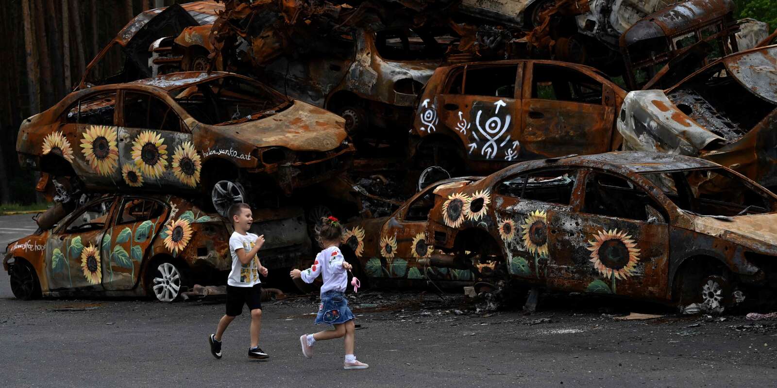 Des enfants jouent devant des voitures détruites par les troupes russes, à Irpine, près de Kiev, le 9 août 2022.