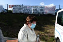 A women wearing a face mask walks as she's helped to get into a vehicle near a banner reading "Hospital under tension, exhausted staff, population in danger, death of the hospital service" in front of the Laval hospital main entrance, northwestern France, on August 21, 2020. - Nurses and caregivers from the service responsible for welcoming Covid-19 patients at Laval hospital have been on indefinite strike since August 19, to demand additional resources. (Photo by JEAN-FRANCOIS MONIER / AFP)