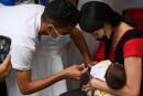 A mother holds her baby while receiving a dose of pentavalent vaccine from medical personnel at a mobile health post set up in Los Caobos park, in Caracas, on August 17, 2022. The government maintains a massive vaccination campaign that began last June, aiming to vaccinate the child population and administer reinforcements against polio, measles, rubella, yellow fever, rotavirus, COVID-19, and others. (Photo by Yuri CORTEZ / AFP)