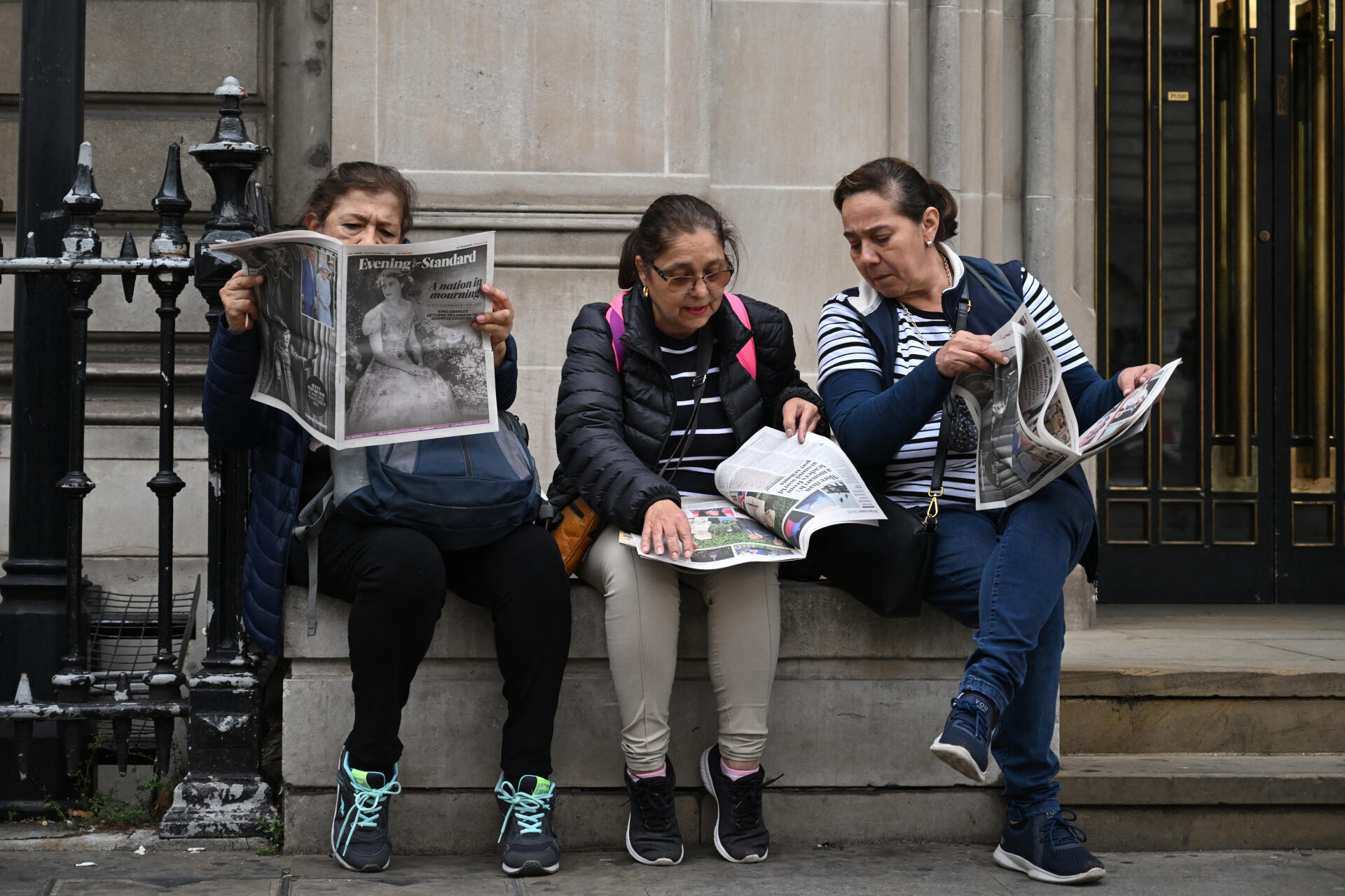 Tres turistas leen un periódico gratuito de Londres, 'The Evening Standard', en el centro de Londres el 9 de septiembre de 2022.