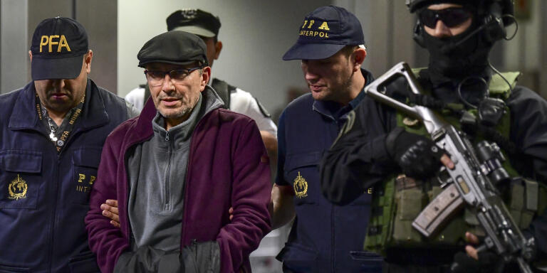 Argentine former police officer Mario Sandoval (2-L) is escorted by police officers upon his arrival at Ezeiza airport in Buenos Aires on December 16, 2019, after France extradited him to face trial over the disappearance of a student. - Argentina suspects that Sandoval took part in more than 500 cases of kidnappings, torture and murder at a time when some 30,000 were 