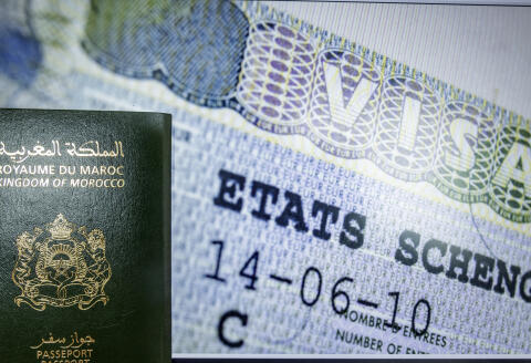 A picture taken on September 28, 2021 in the Moroccan capital Rabat shows a Moroccan passport backdropped against a Schengen visa. - Paris will sharply reduce the number of visas granted to people from Algeria, Morocco and Tunisia, accusing the former French colonies of not doing enough to allow illegal immigrants to return, a government spokesman said today. (Photo by FADEL SENNA / AFP)