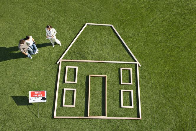 People standing near For sale sign and house outline