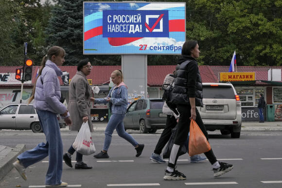 Des habitants de la région de Louhansk passent devant un panneau lumineux où on peut lire « Pour toujours avec la Russie », le 27 septembre 2022.