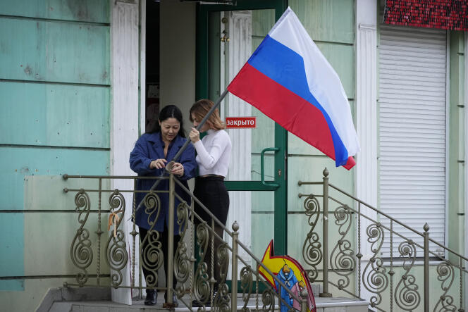 Des femmes accrochent un drapeau russe à leur magasin, à Luhansk, dans l’est de l’Ukraine, mercredi 28 septembre. 2022. 