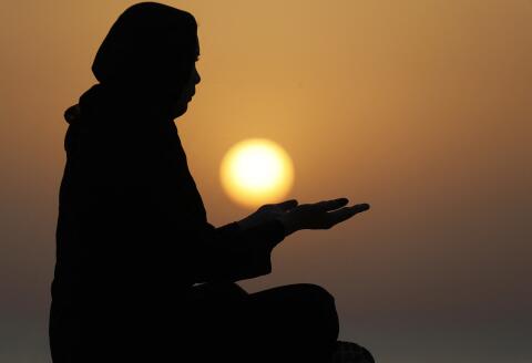 Silhouette of a Muslim woman in abaya praying with her hands at sunset, United Arab Emirates, Middle East