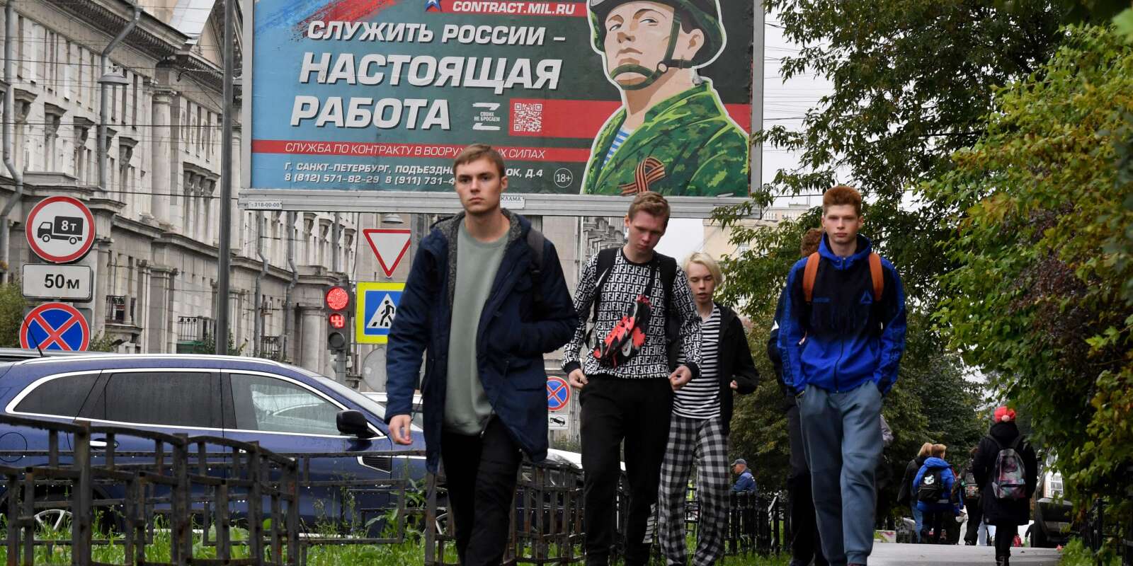 Des jeunes hommes marchent devant un panneau d’affichage faisant la promotion du service militaire à Saint-Pétersbourg le 29 septembre 2022.