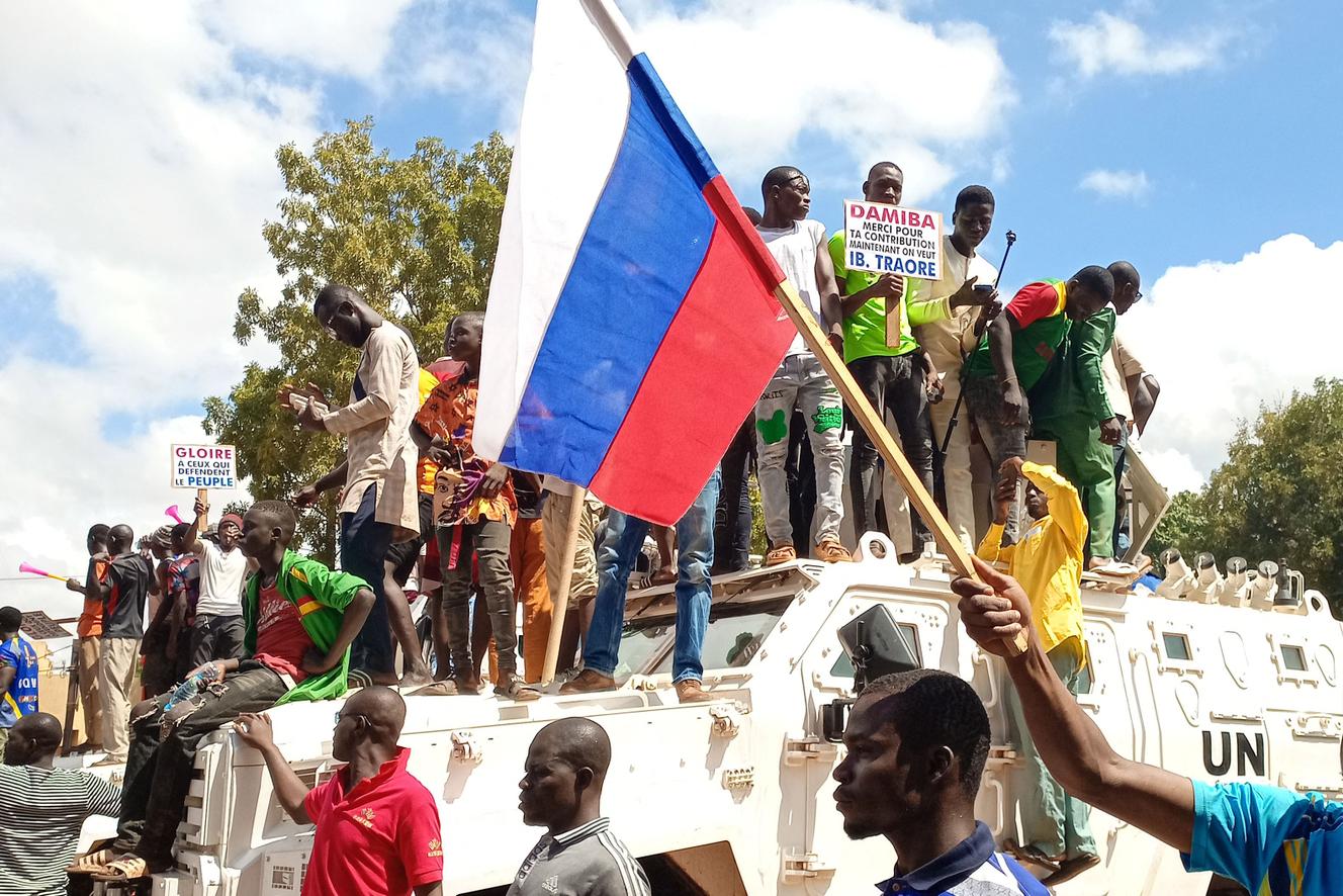 Des manifestants se tiennent debout sur un véhicule blindé des Nations unies, devant un drapeau russe brandi à Ouagadougou, le 2 octobre 2022. (Photo AFP)
