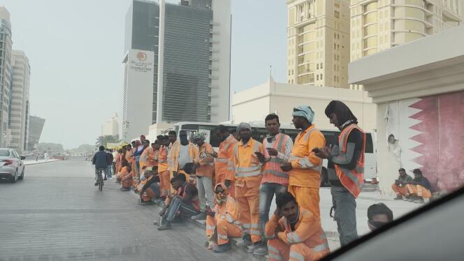 Migrant workers wait on a sidewalk in Doha, Qatar.  The documentary by Pierre-Stéphane Fort and Nicolas Bellot denounces their working conditions on the construction site of the 2022 World Cup.