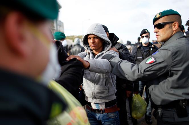 Des personnes venues de Tunisie sont escortées par des agents à leur arrivée sur l’île de Lampedusa, dans le sud de l’Italie, le 30 mars 2011.
