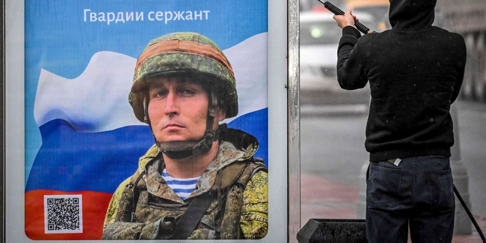 Un ouvrier nettoie une affiche, représentant un soldat russe avec le slogan « Gloire aux héros de la Russie », sur un arrêt de bus à Moscou, le 24 octobre 2022. 