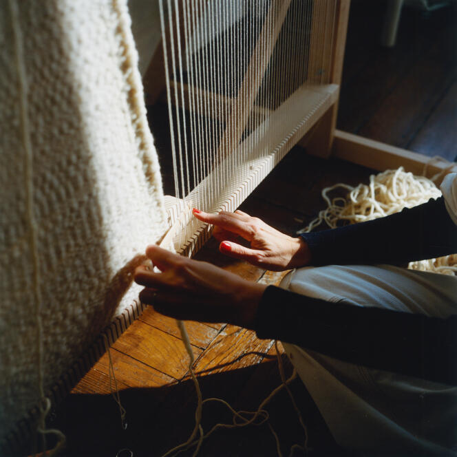 L’artiste tisse en passant l’aiguille en bois, enfilée de laine, dessus-dessous les fils de chaîne tendus à la verticale.