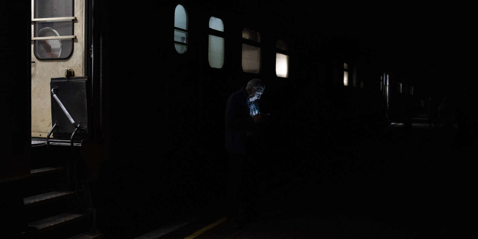 Sur le quai plongé dans le noir de la gare de Kherson, un homme n’est visible que par la lumière de son téléphone. Il s’apprête à prendre un train en direction de Kiev. Le 26 novembre 2022. 