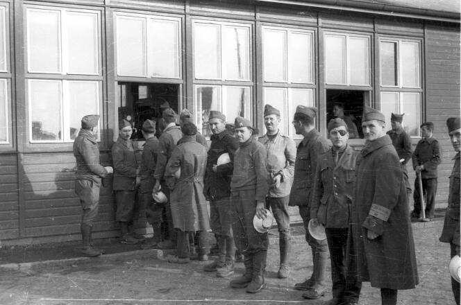 Des prisonniers de guerre français distribuent des repas à la baraque où se trouve la cuisine, le 15 novembre 1940, au camp de Lichterfelde. L’homme avec un brassard (le deuxième en partant de la droite) fait partie de la police du camp.